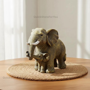Könnte beinhalten: Eine dekorative Elefantenfigur, die einen erwachsenen Elefanten und sein Junges zeigt. Die Figuren sind in Grün- und Brauntönen gehalten, mit weißen Stoßzähnen. Sie stehen auf einer runden, gewebten Matte.