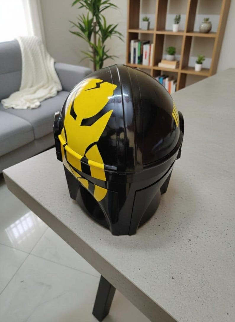 May include: A glossy black helmet featuring a prominent yellow graphic design on the side. The helmet has a smooth, rounded dome shape with a structured visor area and side panels, showcasing a bold contrast between the black and yellow colors.