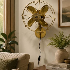 Könnte beinhalten: Ein goldfarbener Wandventilator im Vintage-Stil. Er hat vier Flügel und einen kreisförmigen Käfig. Auf dem Ventilator steht "MADE FOR ROYAL NAVY LONDON". Der Ventilator ist an einer hellen Wand befestigt, mit einem Durchmesser von ca. 40 cm.