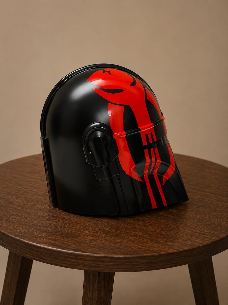 May include: A black helmet featuring a glossy finish and a prominent red graphic design on the front. The design includes a stylized emblem on the forehead area and vertical red stripes extending down the faceplate, with a dark visor section.