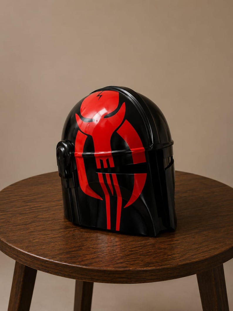 May include: A glossy black helmet featuring a prominent red graphic design on the front. The design depicts a stylized skull-like emblem with sharp, curved lines and a small lightning bolt symbol at the top center of the forehead area.