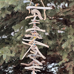 Può includere: Una campanella eolica artigianale in legno di deriva. La campanella presenta più pezzi di legno stagionato disposti verticalmente e collegati con spago. Perline colorate sono sparse nel design. La campanella eolica è appesa a un cordoncino di fibra naturale.