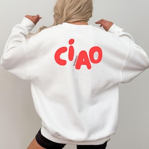 Könnte beinhalten: Weißes Sweatshirt mit dem Wort "CIAO" in großen, roten Buchstaben auf der Rückseite. Das Wort "PATRIARCHY" ist vertikal in kleineren Buchstaben zwischen dem "C" und dem "A" aufgedruckt. Das Sweatshirt hat lange Ärmel und einen Rundhalsausschnitt.