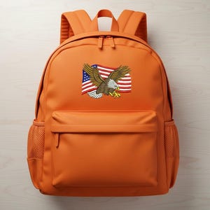 May include: An orange backpack with a front pocket and a mesh side pocket. The backpack has an embroidered design of an American flag and a bald eagle with outstretched wings.