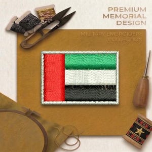 May include: A rectangular embroidered patch featuring the flag of the United Arab Emirates with a vertical red stripe on the left and horizontal green, white, and black stripes on the right, surrounded by a white border on a tan background.