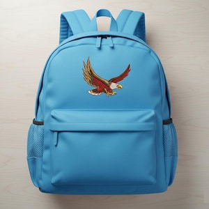 May include: A light blue backpack with a front pocket and side mesh pockets. The backpack features a colorful embroidered eagle design on the front. The eagle has brown, red, and white details.