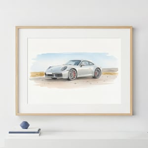 May include: Watercolor painting of a silver sports car with red wheels, set against a backdrop of a light blue sky and tan landscape. The car is framed in a light wood frame.