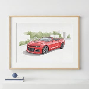 May include: Watercolor print of a red convertible car with black wheels. The car is parked on a paved surface with green foliage and buildings in the background. The artwork is framed in a light wood frame.