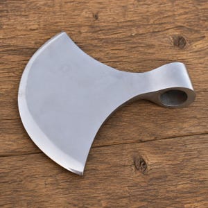 May include: A silver-colored metal axe head with a wide, curved blade and a cylindrical socket for a handle. The surface of the metal is smooth and reflective, featuring a distinct crescent-shaped edge that tapers toward the rounded eye.