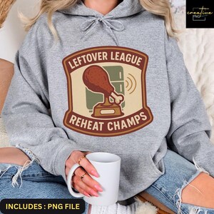以下が含まれることがあります： 「LEFTOVER LEAGUE REHEAT CHAMPS」の文字が入ったグラフィックが特徴のヘザーグレーのパーカー。グラフィックには、漫画のドラムスティックのトロフィーと冷蔵庫が含まれています。パーカーには、ドローストリングフードとフロントポケットが付いています。
