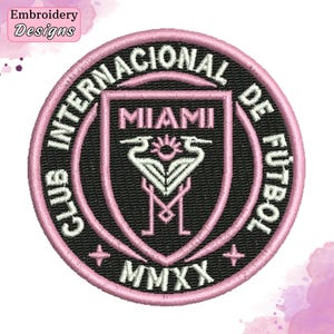 May include: A circular embroidered patch featuring a black background with a pink border. The text reads CLUB INTERNACIONAL DE FUTBOL MIAMI MMXX. The center displays a shield with two white herons facing each other and the letter M below them.