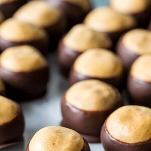 May include: A close-up shot of several peanut butter buckeye candies. Each candy has a round, light brown peanut butter center partially dipped in dark chocolate. The candies are arranged closely together.