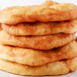 May include: A stack of five golden-brown, fried dough pastries. The pastries have a slightly irregular, circular shape with a lighter, puffy texture. The edges are a darker, caramelized colour, indicating they are freshly cooked.