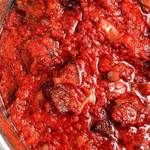 Puede incluir: Primer plano de un guiso rojo vibrante con trozos de carne y cebolla visibles. El plato parece estar hirviendo a fuego lento, con una textura brillante y aceitosa. Los ingredientes están completamente sumergidos en una salsa espesa y sabrosa.