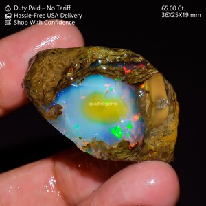 Könnte beinhalten: Ein lebendiger Opal-Edelstein mit einem Gewicht von 65,00 Ct. Der Stein zeigt ein fesselndes Farbspiel, darunter Blau, Grün und Gelb, in einer braunen und beigen Matrix. Abmessungen: 36x25x19 mm.