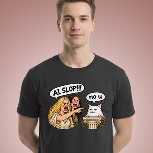 May include: A black short-sleeved t-shirt featuring a graphic print of two angry women pointing at a white cat sitting on a pedestal. The speech bubble above the women says AI SLOP!!! and the speech bubble above the cat says no u.
