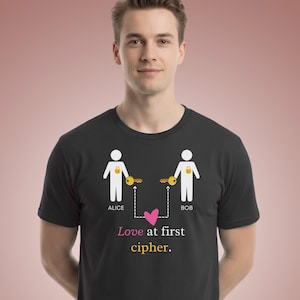 May include: A black t-shirt featuring a graphic of two white stick figures labeled Alice and Bob. Each figure has a gold padlock on their chest and holds a gold key. A dashed line connects the keys to a pink heart, with the text Love at first cipher.