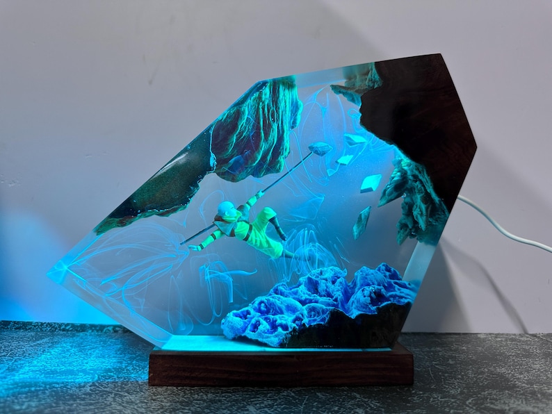 May include: A unique resin art piece featuring a diver in a neon green suit, suspended in a clear, glowing blue environment. The artwork includes blue coral and rock formations, set on a wooden base. The piece is illuminated with a blue light.