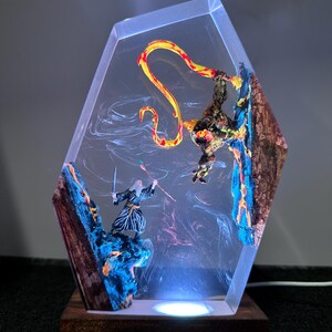 Puede incluir: Una escultura de resina de tem&aacute;tica fant&aacute;stica que representa a un mago luchando contra un drag&oacute;n. La pieza hexagonal transparente tiene una base de madera e iluminaci&oacute;n LED interna. El mago sostiene una espada y un bast&oacute;n, mientras que el drag&oacute;n es rojo y amarillo.