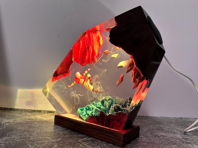 May include: A unique resin lamp with a wood base and accents. The lamp features a figure suspended in the resin, with red and green elements. The lamp has a warm glow and a white power cord.