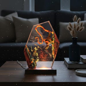 Puede incluir: L&aacute;mpara decorativa con forma hexagonal, con un dise&ntilde;o detallado de resina que representa una figura de guerrero y un drag&oacute;n. La l&aacute;mpara tiene una base de madera y emite un brillo c&aacute;lido y acogedor. La obra de arte interior es una mezcla de rojo, naranja y verde.