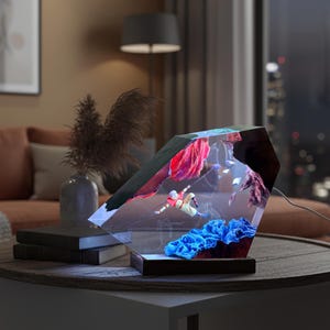 May include: A decorative, geometric-shaped lamp with an underwater scene illuminated inside. The lamp features a diver, red and blue coral, and other aquatic elements. The lamp sits on a round table with a dark wood base.