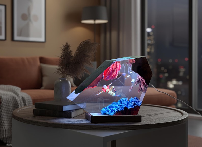 May include: A decorative, geometric-shaped lamp with an underwater scene illuminated inside. The lamp features a diver, red and blue coral, and other aquatic elements. The lamp sits on a round table with a dark wood base.