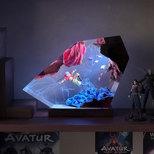 May include: A decorative resin sculpture featuring a figure in mid-air, suspended within a clear, angled structure. The sculpture includes red and blue elements, with a wooden base. Additional figurines are visible on a shelf.