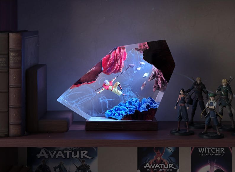 May include: A decorative resin sculpture featuring a figure in mid-air, suspended within a clear, angled structure. The sculpture includes red and blue elements, with a wooden base. Additional figurines are visible on a shelf.