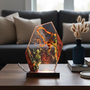 Puede incluir: L&aacute;mpara decorativa con un dise&ntilde;o &uacute;nico. La l&aacute;mpara presenta un cuerpo de resina transparente y hexagonal con un dise&ntilde;o interno de un guerrero y un drag&oacute;n. La base es de madera oscura y la l&aacute;mpara emite un brillo c&aacute;lido y acogedor.