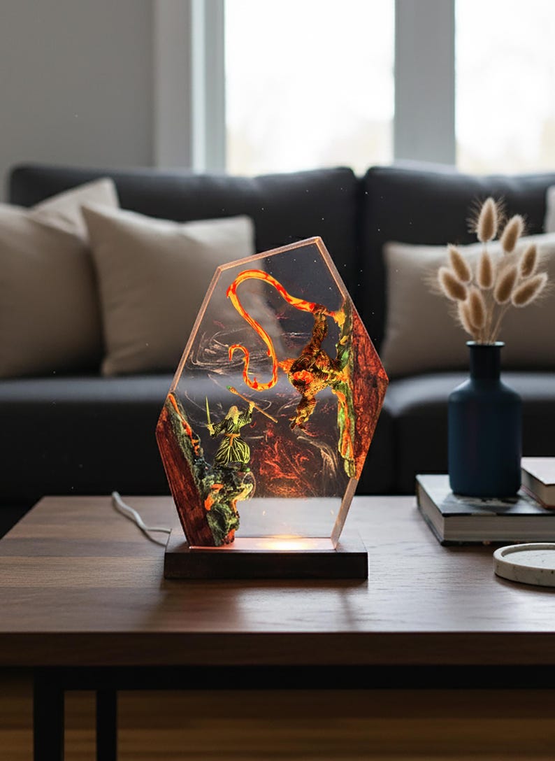 Puede incluir: L&aacute;mpara decorativa con un dise&ntilde;o &uacute;nico. La l&aacute;mpara presenta un cuerpo de resina transparente y hexagonal con un dise&ntilde;o interno de un guerrero y un drag&oacute;n. La base es de madera oscura y la l&aacute;mpara emite un brillo c&aacute;lido y acogedor.