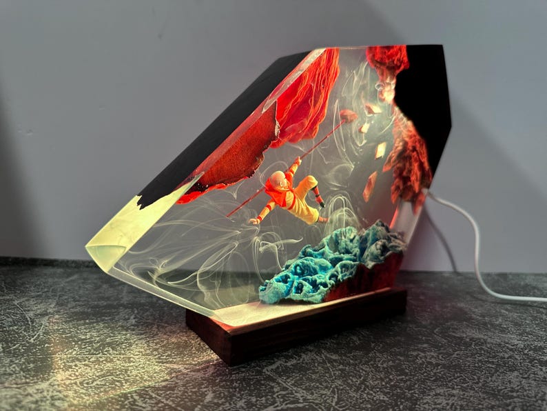 May include: A unique resin lamp featuring a miniature figure in an orange suit climbing a red rock formation. The lamp has a wooden base and a clear, angled body with a black top. The scene includes blue and red elements.