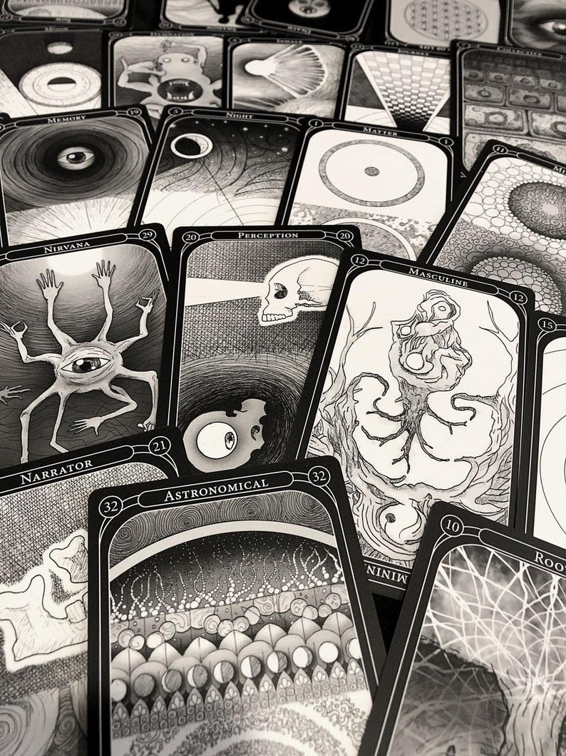 May include: A collection of black and white tarot cards with intricate illustrations. The cards feature surreal imagery, including eyes, skulls, and abstract designs. Text on the cards includes words like "Nirvana," "Perception," and "Astronomical."