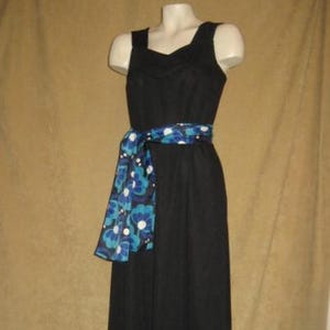 May include: A black sleeveless dress with a square neckline and a long, flowing skirt. A blue and white floral patterned sash is tied around the waist. The dress is displayed on a mannequin.