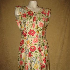 May include: A vintage floral print dress with a scoop neckline and a fitted waist. The dress features a cream-colored background with a vibrant pattern of red, pink, and blue flowers, and green leaves. The dress is displayed on a mannequin.