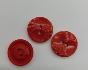 May include: Three red plastic buttons with a raised design. Two buttons have a swirl design and one button is smooth.