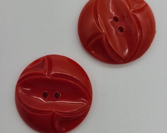 May include: Two red plastic buttons with a decorative design. Each button has two holes.