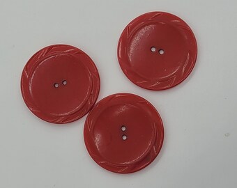 May include: Three red plastic buttons with two holes each. The buttons have a decorative design around the edge.