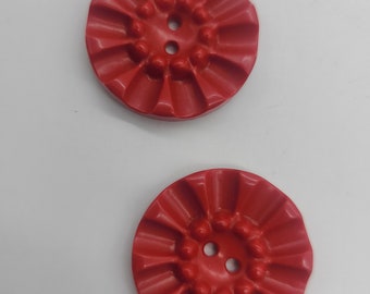 May include: Two red plastic buttons with a ruffled edge and two holes.