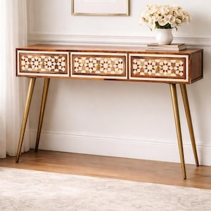 Può includere: Una consolle in legno con tre cassetti con un intarsio geometrico nei toni del marrone e crema. I cassetti hanno pomelli color oro. Il tavolo poggia su quattro sottili gambe in metallo color oro, aggiungendo un tocco di eleganza. Misure in cm.