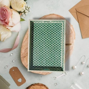 Könnte beinhalten: Rechteckige dekorative Tablett mit einem grün-weißen Schuppenmuster. Das Tablett hat einen hellfarbigen Holzrahmen. Das Bild enthält auch einen Strauß aus rosa und weißen Rosen, Ohrringe und ein Geschenkanhänger.