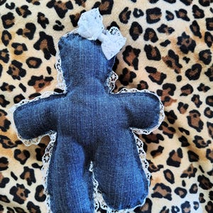 May include: A handmade denim doll with a white lace trim and a white lace bow. The doll is in the shape of a person and is made of blue denim fabric. The doll is laying on a leopard print background.