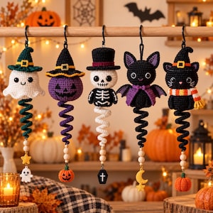 May include: Five crocheted Halloween hanging ornaments featuring a ghost in a green hat, a purple pumpkin in a black hat, a skeleton in a top hat, a black bat with purple wings, and a black cat in a witch hat, all with spiral tails and charms.