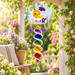 May include: A hanging crochet mobile featuring a yellow crescent moon with a purple nightcap, a white cloud with a smiling face, and a purple flower. Below, a rainbow-colored spiral tail hangs with small purple stars and a clear crystal prism.