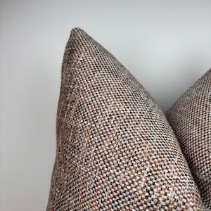 May include: Close-up of two decorative throw pillows. The pillows have a textured woven fabric in a brown, black, and white color scheme. The pillows are in a triangular shape, with a seam running down the center.