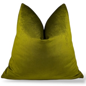 Puede incluir: Un gran cojín de terciopelo verde oliva. El cojín es de color liso y tiene un aspecto suave y afelpado. El cojín es un elemento decorativo, probablemente para un sofá o una cama.