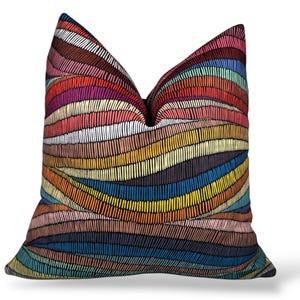 May include: A decorative throw pillow with a vibrant, abstract design. The pillow features a pattern of colorful, horizontal stripes in shades of red, orange, yellow, blue, and purple. The design has a textured, hand-stitched appearance, adding visual interest.