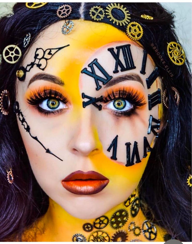 May include: A face painted with a clock face design featuring black Roman numerals, clock hands, and metallic gear accents on the skin and hair. The makeup includes vibrant yellow and orange tones, long eyelashes, and metallic copper lipstick.