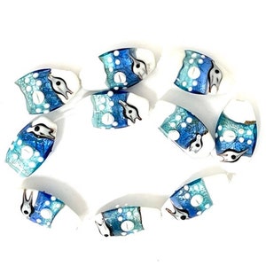 May include: A collection of ten white oval glass beads with blue and silver accents. Each bead features a stylized dolphin design.