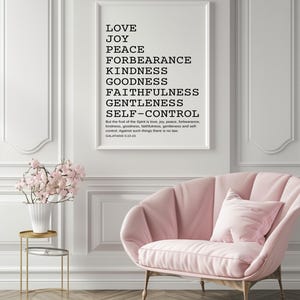 Pode incluir: Uma impressão emoldurada com as palavras "LOVE, JOY, PEACE, FORBEARANCE, KINDNESS, GOODNESS, FAITHFULNESS, GENTLENESS, SELF-CONTROL" em texto preto. Uma poltrona rosa e uma pequena mesa lateral dourada com um vaso de flores rosas estão em primeiro plano.